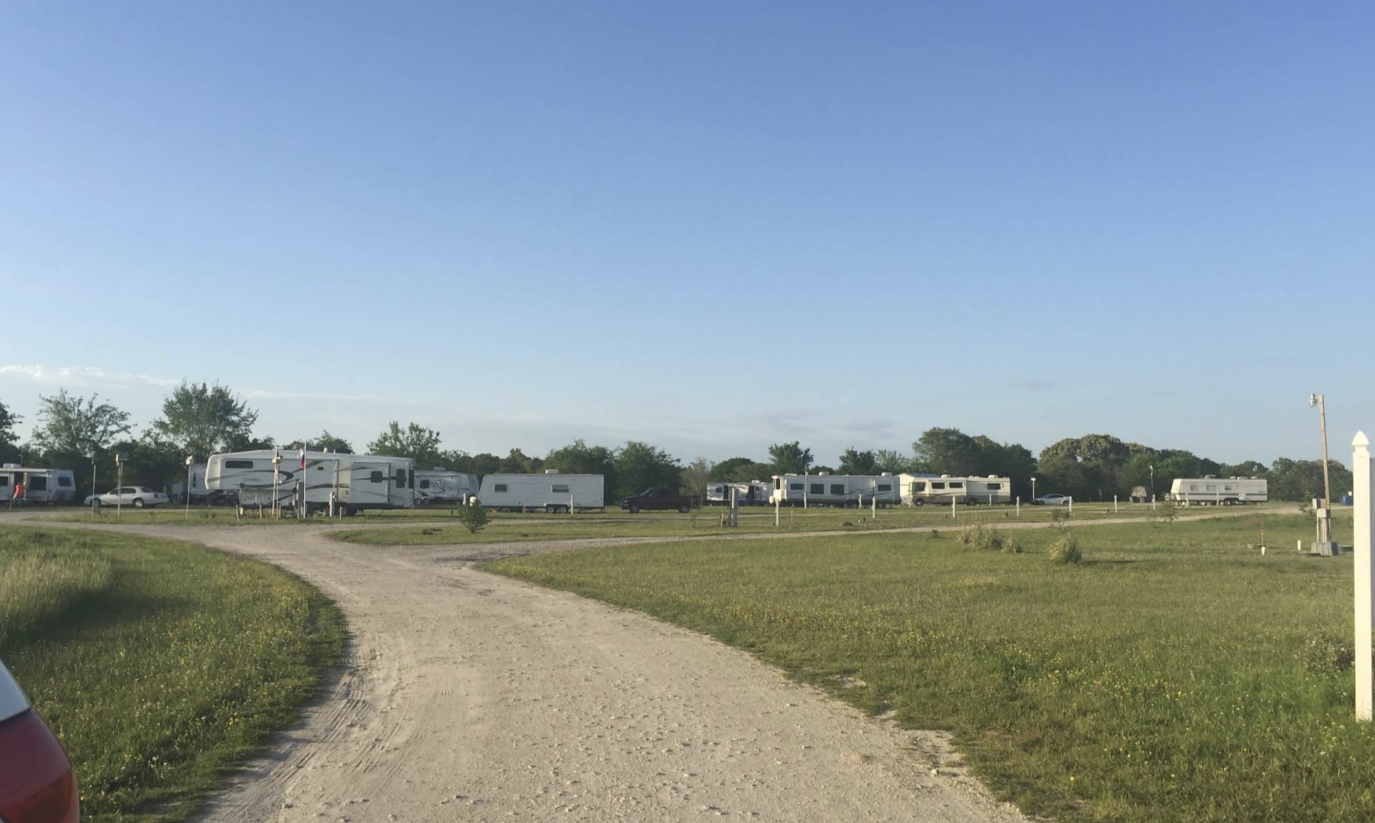 Gravel drive through a grassy field of travel trailers and fifth-wheels at Lone Star RV Ranch.